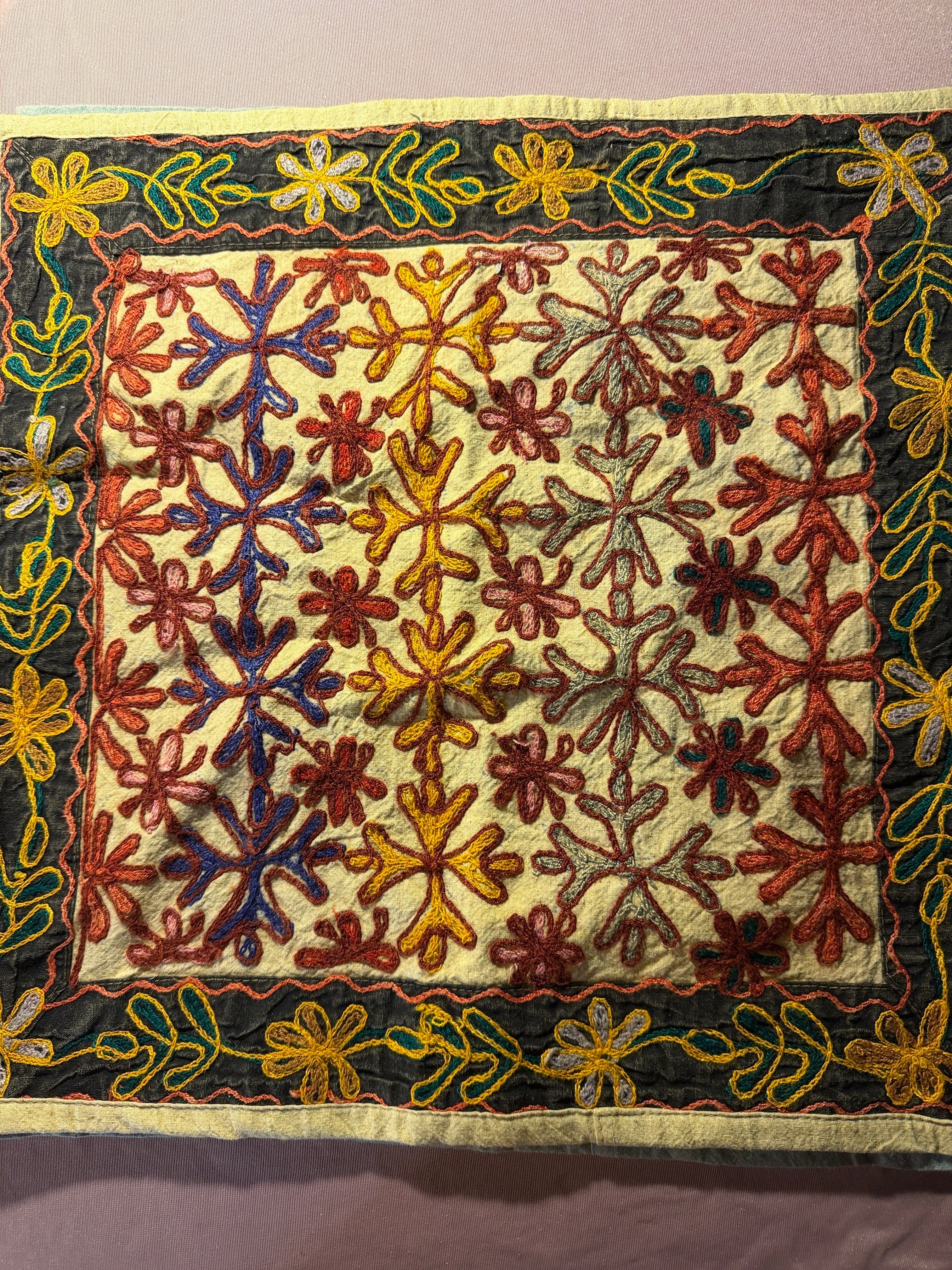 Colorful handmade embroidered textile with floral and snowflake patterns on cream background with dark embroidered border